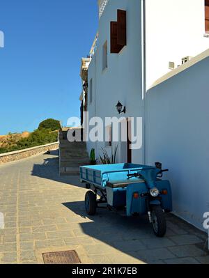 Ein blaues altes Motorrad mit Beiwagen steht in einer Dorfstraße in Lindos. In der Nähe der weißen Wände eines Hauses mit Holzläden und einer Tür. Stockfoto