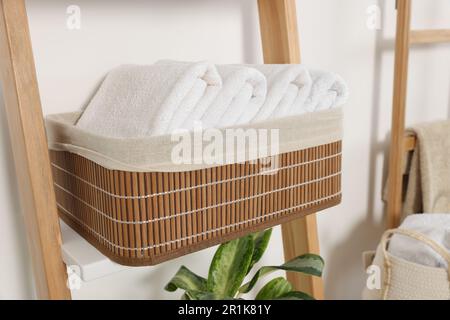 Weiche Handtücher in Korb aus Korb auf dekorativer Leiter nahe der weißen Wand Stockfoto