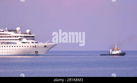 Schiffe, Kreuzfahrtschiffe, Vergnügungsboote liegen im Hafen der griechischen Insel vor. Mehrstöckige Auskleidungen. Marine-Traktor zieht die Auskleidung. Stockfoto