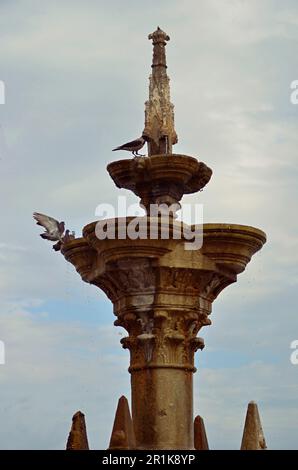 Mittelalterlicher Steinbrunnen am Himmel. Mehrere Tauben fliegen um den Brunnen. Stockfoto