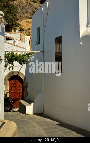 Eingangstüren zu den Häusern des Kapitäns im Dorf Lindos auf der Insel Rhodos. Weiße Wände, Holzbogentüren und der Felsen der Akropolis Stockfoto