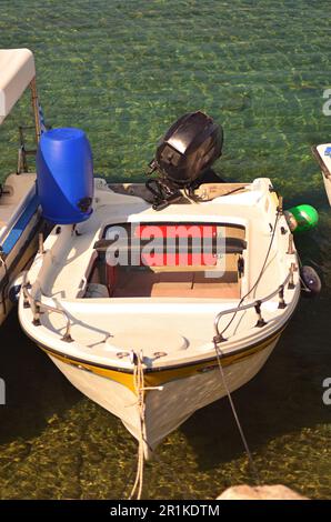 Ein kleines Motorboot ohne Baldachin ist in flachem Wasser neben anderen Booten verankert. Tirquoise klares Wasser in der Bucht der Insel Stockfoto