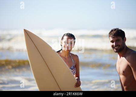 Unser Sommer. Porträtaufnahme eines glücklichen jungen Paares, das mit einem Surfbrett im Meer posiert. Stockfoto