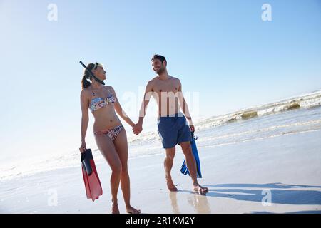 Kurzurlaub für einen tollen Urlaub. Ein junges Paar spaziert zusammen mit Schnorchelausrüstung am Strand entlang. Stockfoto