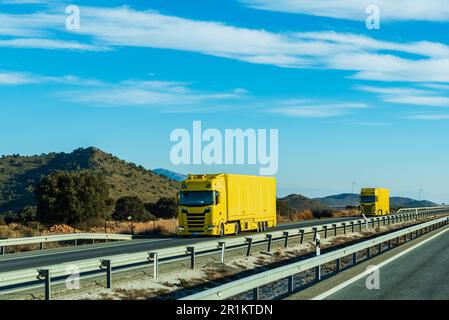 Zwei Lkw mit ihren gelben Anhängern, die zusammen auf der Autobahn fahren. Stockfoto