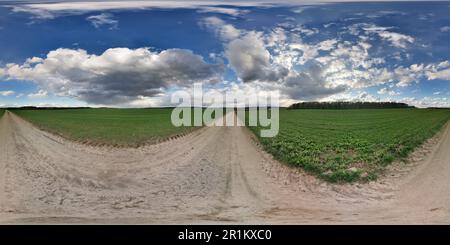 Vollständiges, nahtloses, kugelförmiges Hdri Panorama 360°-Blickwinkel auf ländlicher Schotterstraße zwischen Feldern im Frühling mit überwältigenden Wolken in rechteckiger Pr Stockfoto