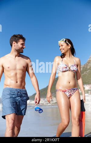 Wir lieben es, unser Lieblingshobby zu teilen. Ein junges Paar spaziert zusammen mit Schnorchelausrüstung am Strand entlang. Stockfoto