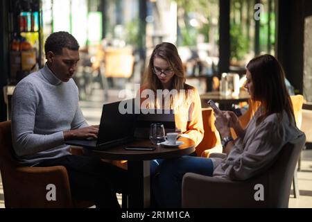 Drei multirassische Geschäftskollegen, die nach der Arbeit oder während einer Kaffeepause in einem Restaurant ein Meeting abhalten. Freunde, die in einer Café-Bar arbeiten. Stockfoto