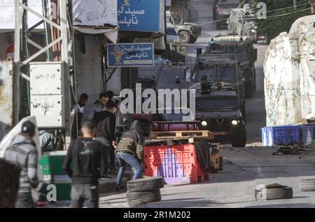 Nablus, Palästina. 14. Mai 2023. Ein palästinensischer Jugendlicher wirft während des Überfalls in der Stadt Nablus Steine auf die Fahrzeuge der israelischen Armee, um einige gesuchte Personen von den israelischen Behörden östlich von Nablus im besetzten Westjordanland zu verhaften. Kredit: SOPA Images Limited/Alamy Live News Stockfoto