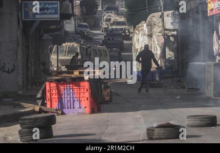 Nablus, Palästina. 14. Mai 2023. Ein palästinensischer Jugendlicher wirft während des Überfalls in der Stadt Nablus Steine auf die Fahrzeuge der israelischen Armee, um einige gesuchte Personen von den israelischen Behörden östlich von Nablus im besetzten Westjordanland zu verhaften. (Foto von Nasser Ishtayeh/SOPA Images/Sipa USA) Guthaben: SIPA USA/Alamy Live News Stockfoto