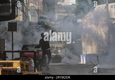 Nablus, Palästina. 14. Mai 2023. Ein palästinensischer Jugendlicher wirft während des Überfalls in der Stadt Nablus Steine auf die Fahrzeuge der israelischen Armee, um einige gesuchte Personen von den israelischen Behörden östlich von Nablus im besetzten Westjordanland zu verhaften. (Foto von Nasser Ishtayeh/SOPA Images/Sipa USA) Guthaben: SIPA USA/Alamy Live News Stockfoto
