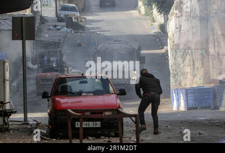 Nablus, Palästina. 14. Mai 2023. Ein palästinensischer Jugendlicher wirft während des Überfalls in der Stadt Nablus Steine auf die Fahrzeuge der israelischen Armee, um einige gesuchte Personen von den israelischen Behörden östlich von Nablus im besetzten Westjordanland zu verhaften. (Foto von Nasser Ishtayeh/SOPA Images/Sipa USA) Guthaben: SIPA USA/Alamy Live News Stockfoto