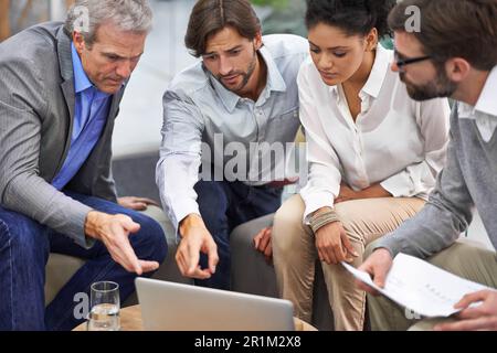 Können wir so etwas auf unserer Website machen? Eine vielfältige Gruppe von Büromitarbeitern, die sich um ein Notebook unterhalten. Stockfoto