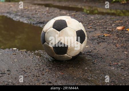 Dreckiger Fußball in der Nähe der Pfütze auf dem Boden Stockfoto