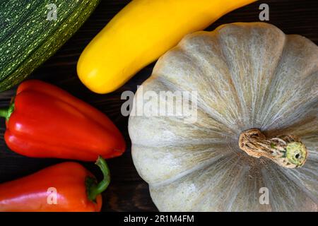 Kürbis und Gemüsemark auf dunklem Holztisch, Draufsicht. Stillleben von Bio-Lebensmitteln, süßer roter Pfeffer und Zucchini, flach liegend. Ernte, Gemüse, Stockfoto