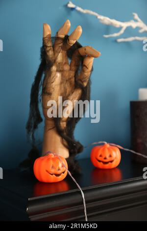 Jack-o'-Laternen-Lampen und Holzhand am schwarzen Kamin in der Nähe der blauen Wand Stockfoto