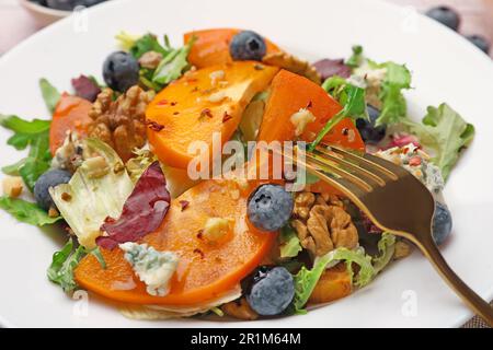 Köstlicher Persimonsalat und Gabel auf weißem Teller, Nahaufnahme Stockfoto