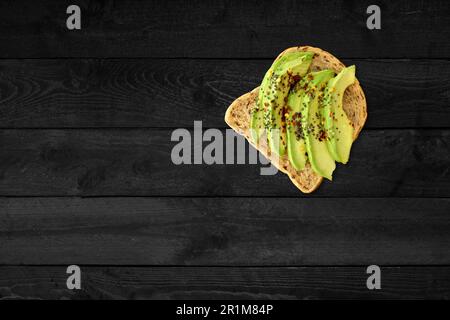 Nahaufnahme des Avocado-Sandwichs isoliert auf einem schwarzen Holztisch. Stockfoto