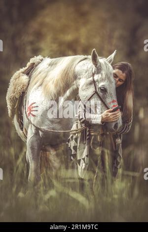 Porträt einer Frau auf ihrer amerikanischen Kriegsbemalung, dekoriert weißes arabisches Pferd im Frühling draußen Stockfoto