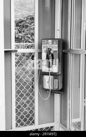 Ein altes, funktionierendes Münztelefon hängt an einem öffentlichen Rastplatz in New Hampshire. Dieses Bild wurde auf analogem Schwarzweißfilm aufgenommen. Stockfoto