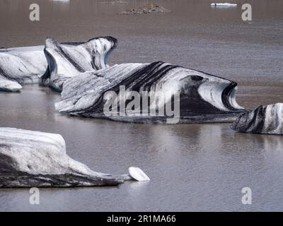 Eine malerische Szene eines ruhigen Sees mit mehreren großen, gebogenen und zerklüfteten Eisstücken, die im Wasser schweben Stockfoto