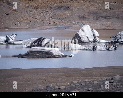 Eine malerische Szene eines ruhigen Sees mit mehreren großen, gebogenen und zerklüfteten Eisstücken, die im Wasser schweben Stockfoto