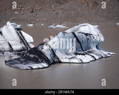 Eine malerische Szene eines ruhigen Sees mit mehreren großen, gebogenen und zerklüfteten Eisstücken, die im Wasser schweben Stockfoto