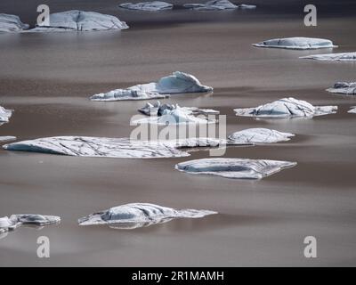 Eine malerische Szene eines ruhigen Sees mit mehreren großen, gebogenen und zerklüfteten Eisstücken, die im Wasser schweben Stockfoto
