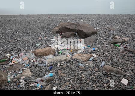 Müll verstreut auf Kieselsteinen nahe dem Meer. Recycling-Problem Stockfoto