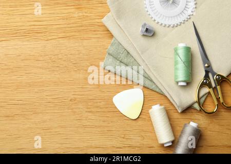 Flache Liegezusammensetzung mit Gewindespule und Nähwerkzeugen auf Holztisch. Platz für Text Stockfoto