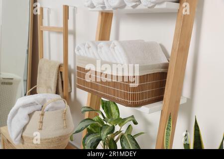 Weiche Handtücher in Korb aus Korb auf dekorativer Leiter nahe der weißen Wand Stockfoto