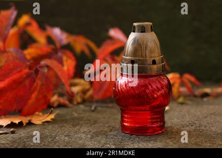 Rote Grablaterne und heruntergefallene Blätter auf einer Steinoberfläche auf dem Friedhof, Platz für Text Stockfoto