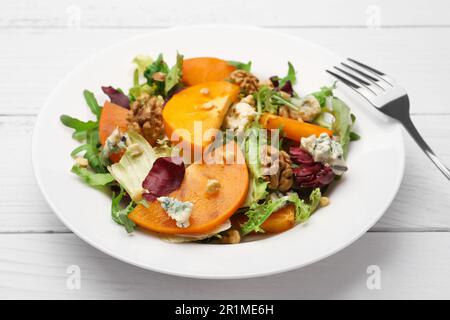 Köstlicher Persimonsalat und Gabel auf weißem Holztisch, Nahaufnahme Stockfoto