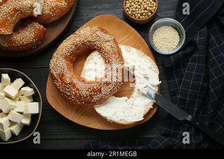 Köstlicher Bagel mit Tofu-Frischkäse und Sojabohnen auf schwarzem Holztisch, flach liegend Stockfoto