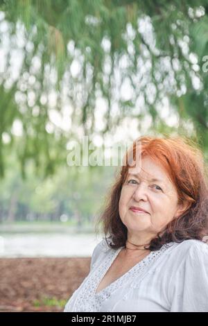 Porträt einer lateinischen Seniorin, die sorglos lächelt und in die Natur schaut. Helle Komposition mit Kopierbereich. Konzept: Sorgenfrei und happ Stockfoto