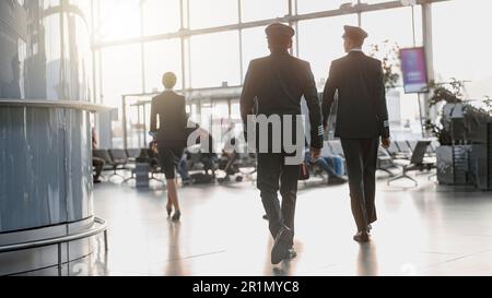 Zwei Piloten, die der Stewardess am Flughafenterminal entlang laufen Stockfoto