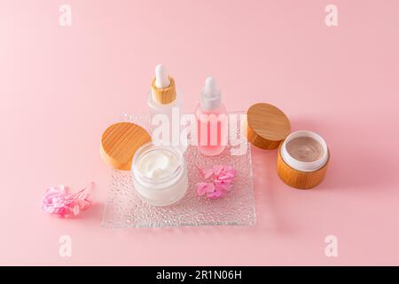 Zwei matte Tropfflaschen und zwei offene Gläser mit Creme für eine natürliche häusliche Pflege der Gesichts- und Körperhaut. Natürliche Kosmetik. Stockfoto