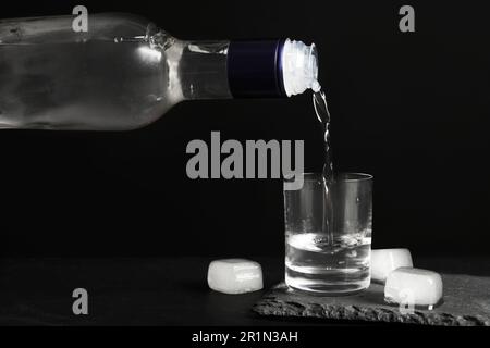 Wodka aus der Flasche in Glas und Eiswürfel auf dem schwarzen Tisch Stockfoto