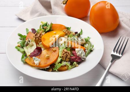 Köstlicher Persimonsalat und Gabel auf weißem Holztisch Stockfoto