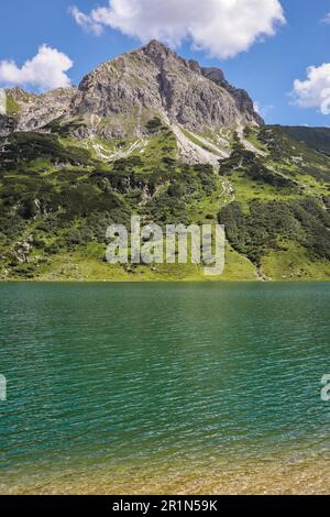 Vertikaler Blick auf den wunderschönen Rocky Peak auf einem grünen Hügel mit Alpensee. Tappenkarsee mit einem Berg am Sommertag in Osterreich. Stockfoto