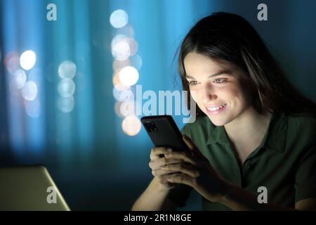 Eine Frau in der Nacht zu Hause, die ihr Handy überprüft Stockfoto