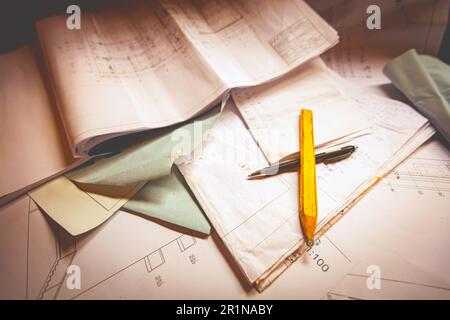 Der quadratische Holzbleistift aus Graphit und chemischer Rollstift von Maurer sind mit einer Reihe von architektonischen Bauplänen, Plänen und Zeichnungen durchkreuzt. Stockfoto