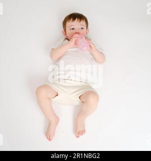 Happy Baby trinkt Milch aus der Flasche auf weißem Studiohintergrund. Ruhendes Kind isst Formel. Kind etwa zwei Jahre alt (ein Jahr neun Monate) Stockfoto