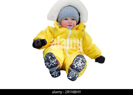 Ein kleiner Junge in einem gelben Schneeanzug fährt auf einem verschneiten Spielplatz, isoliert auf weißem Hintergrund, eine Kinderrutsche hinunter. Kind im Alter von einem Jahr und fünf Monaten Stockfoto