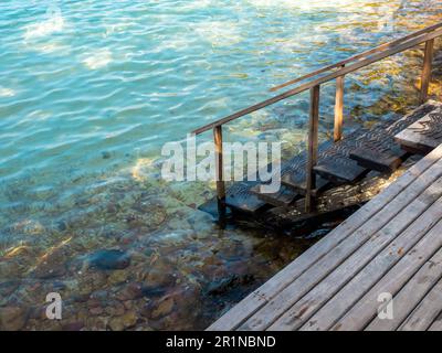 Weg zum Meer. Leere Holztreppen auf der Holzplanke Terrasse am Strand, Felsen und blauer entspannender Meerwasserhintergrund. Sommerurlaub und Urlaub Stockfoto