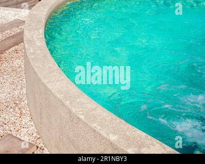 Geschwungene Steinfassade am Pool in der Nähe des Aqua Blue Water Pools mit Wasserdruck im Swimmingpool an sonnigen Tagen mit Kopie sp Stockfoto