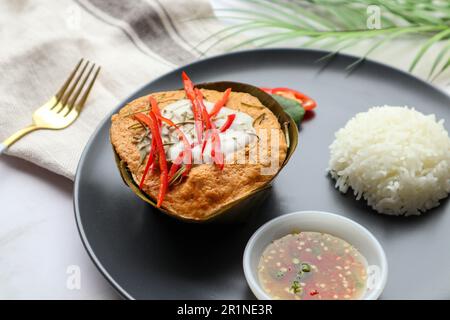 Gedämpftes Fisch-Curry in Bananenblattbechern serviert mit weißem Reis und würziger Fischsauce - berühmte thailändische Gerichte namens Hor Mok oder Fish Amok aus nächster Nähe Stockfoto