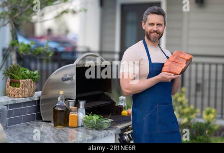 Koch-Mann, der Lachs auf dem Grill im Freien kocht, Banner. Lachsfisch grillen, Mann trägt Schürze. Stockfoto