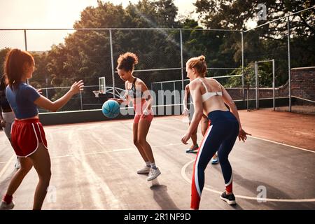 Druck wird hinzugefügt. Eine vielfältige Gruppe von Sportlerinnen, die tagsüber gemeinsam ein Wettkampfspiel mit Basketball spielen. Stockfoto