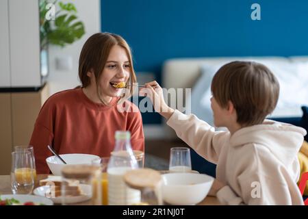 Glückliche Kinder Geschwister, die Spaß miteinander haben, Frühstücksflocken essen, Bruder, die Schwestern Cornflakes füttern Stockfoto